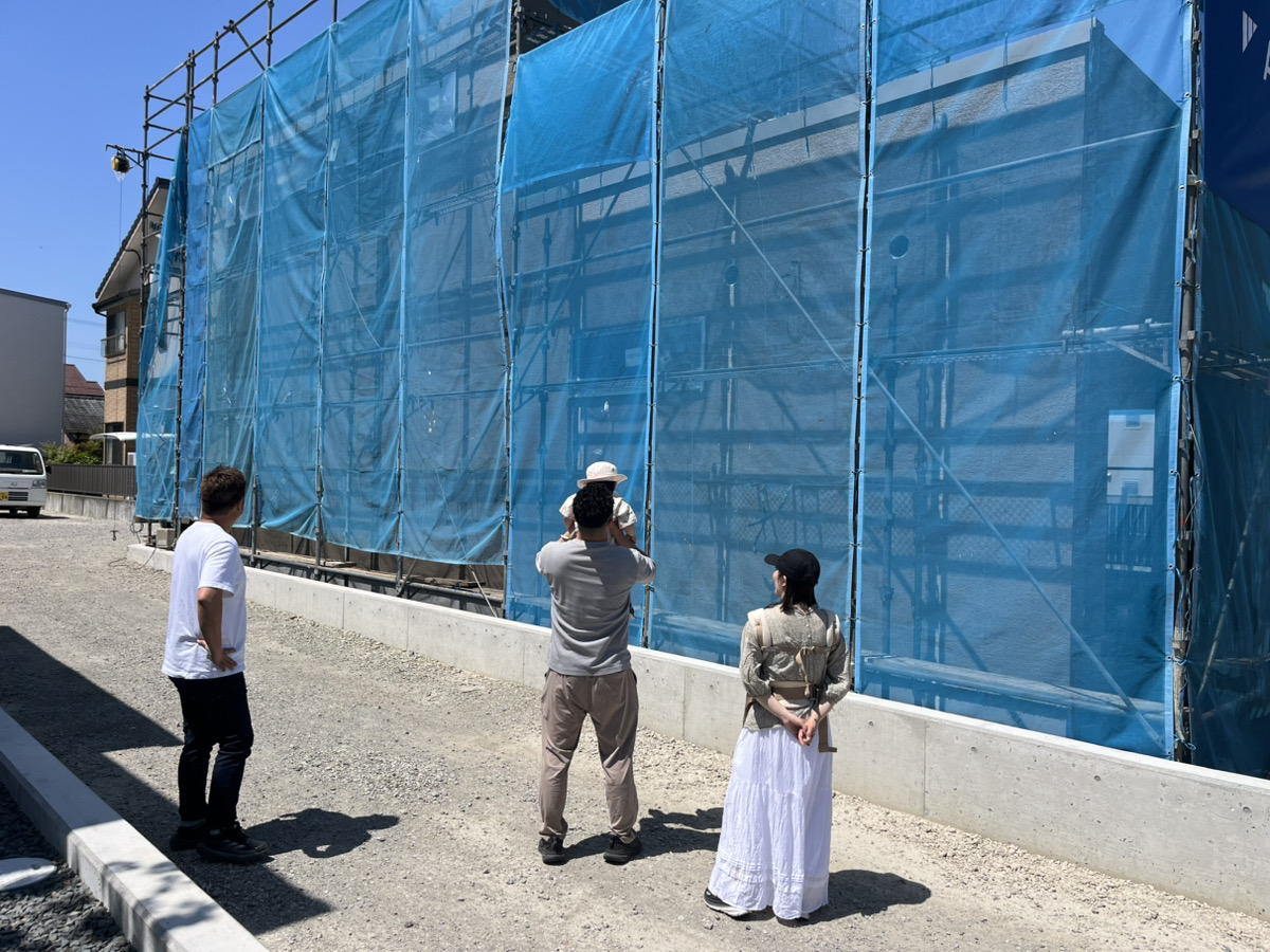 足場が組まれた宇和島市御徒町YN様邸の外観を見上げるご家族の様子