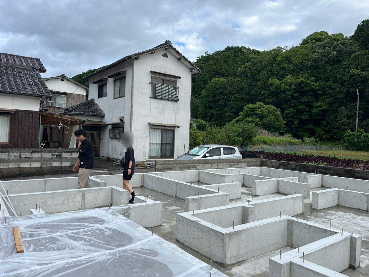 RO様ご夫婦が、基礎コンクリートの立ち上がりの間を歩きながら新居の間取りを確認している様子