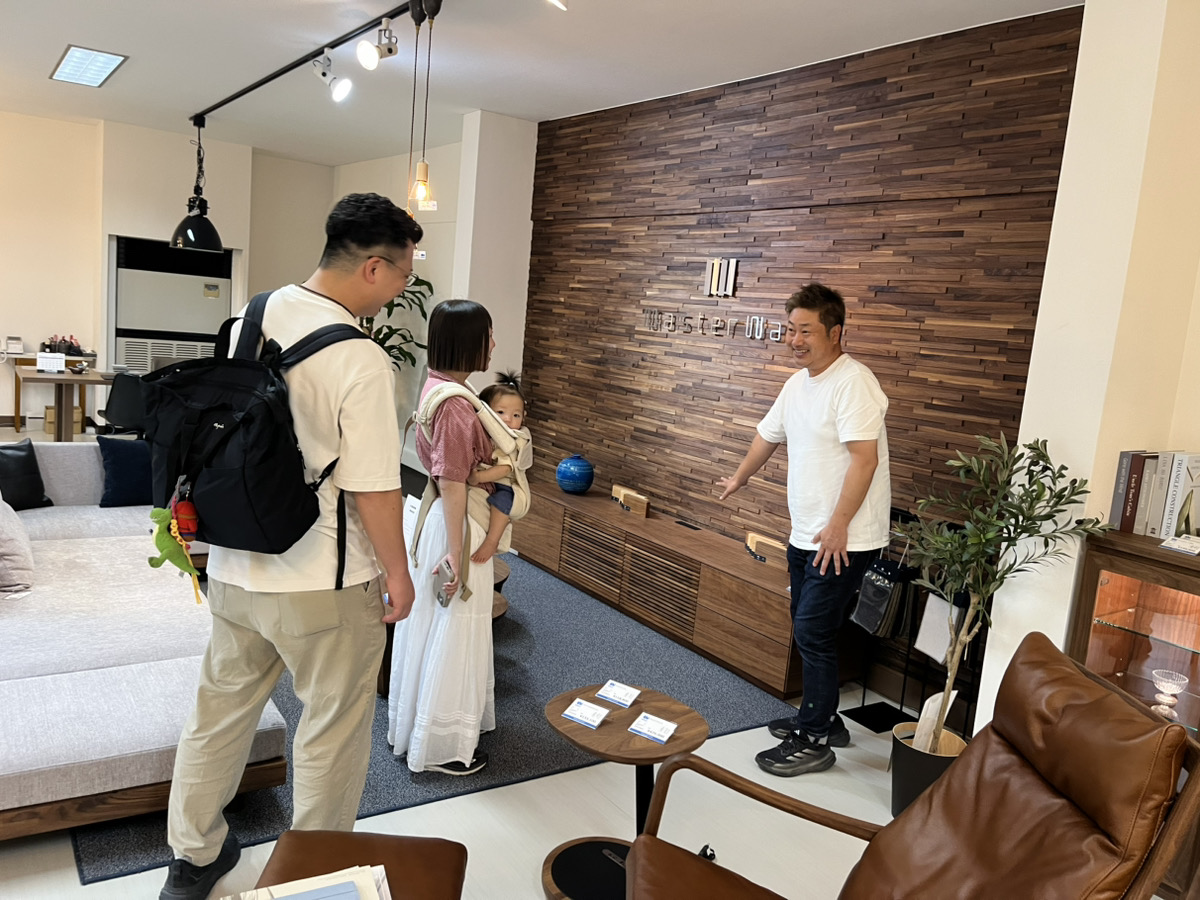 家具店「家具の丸三」のショールームで、YN様ご家族に生活動線やテレビボードのサイズ感を提案するスタッフの様子