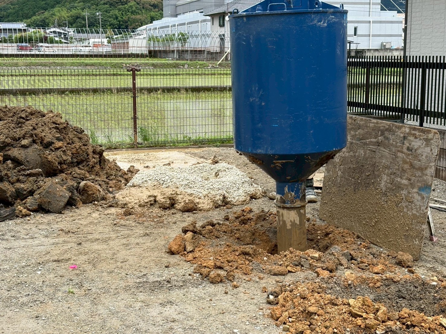 地盤改良工事で柱状に掘削された穴の上に設置された青いホッパー（砕石投入用治具）