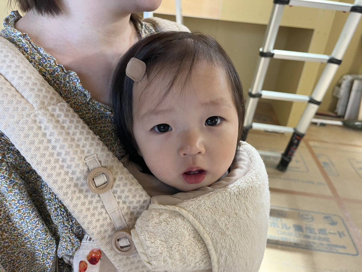 お母さんに抱っこ紐で抱かれながら、ぱっちりとした目で現場を見つめる可愛らしい女の子