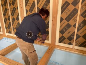 施工スタッフが床の土台まわりにウレタンフォームを打ち込み、基礎断熱の気密処理を行っている様子。壁面にはLIXILのSWパネルが施工済み。